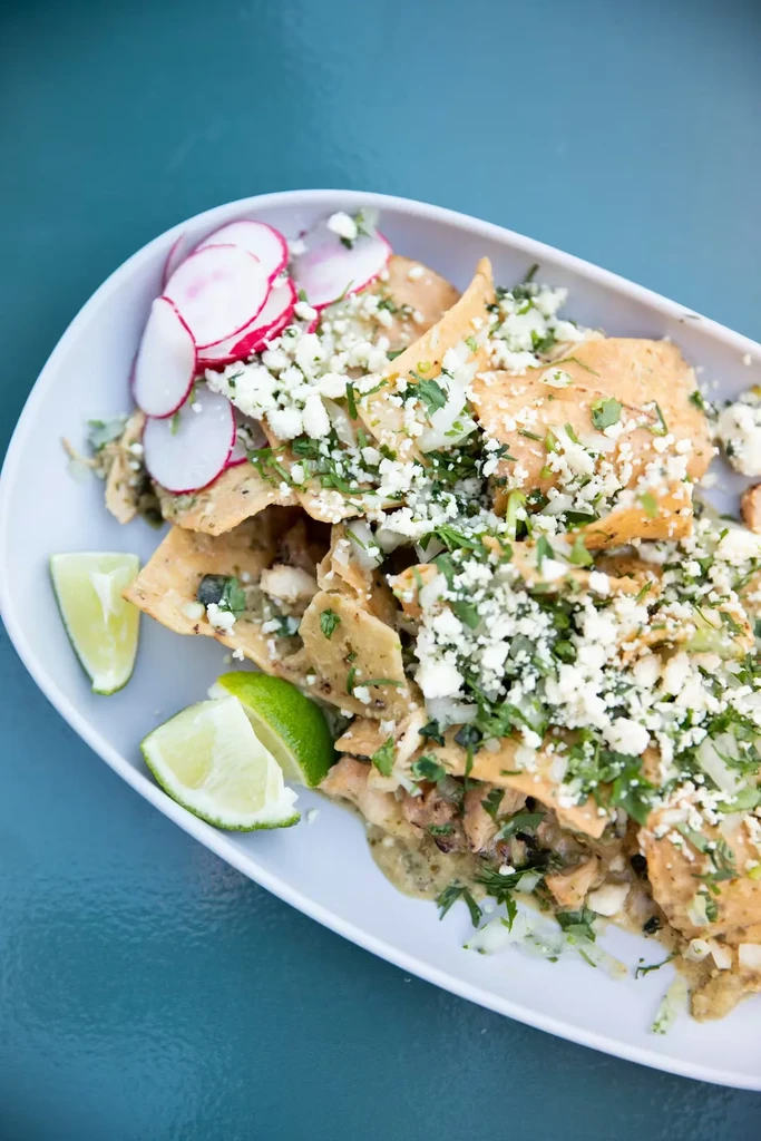 Overhead chilaquiles verde, cheese, herbs, radishes, and lime.