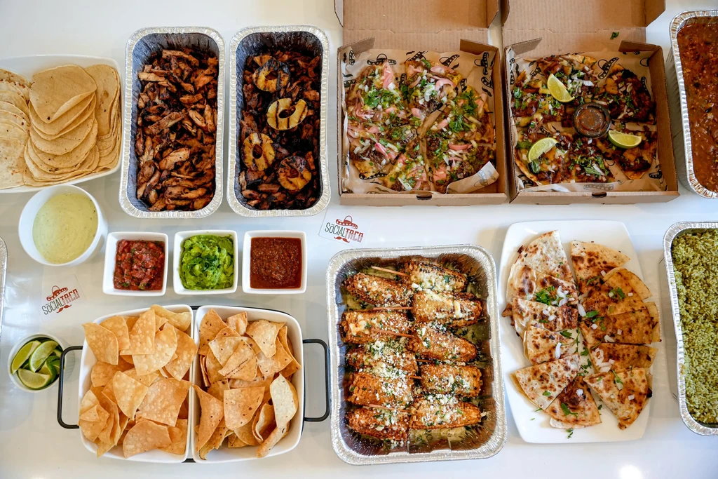 Abundant flat-lay of Mexican food, including tacos, elote, and salsas.