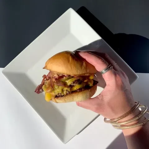 Hand holding a double-patty burger with melted cheese and onions.