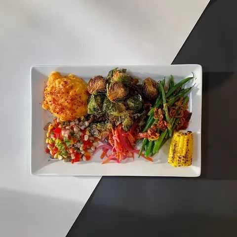 White plate with roasted vegetables, bean salad, spiced puree, and corn.