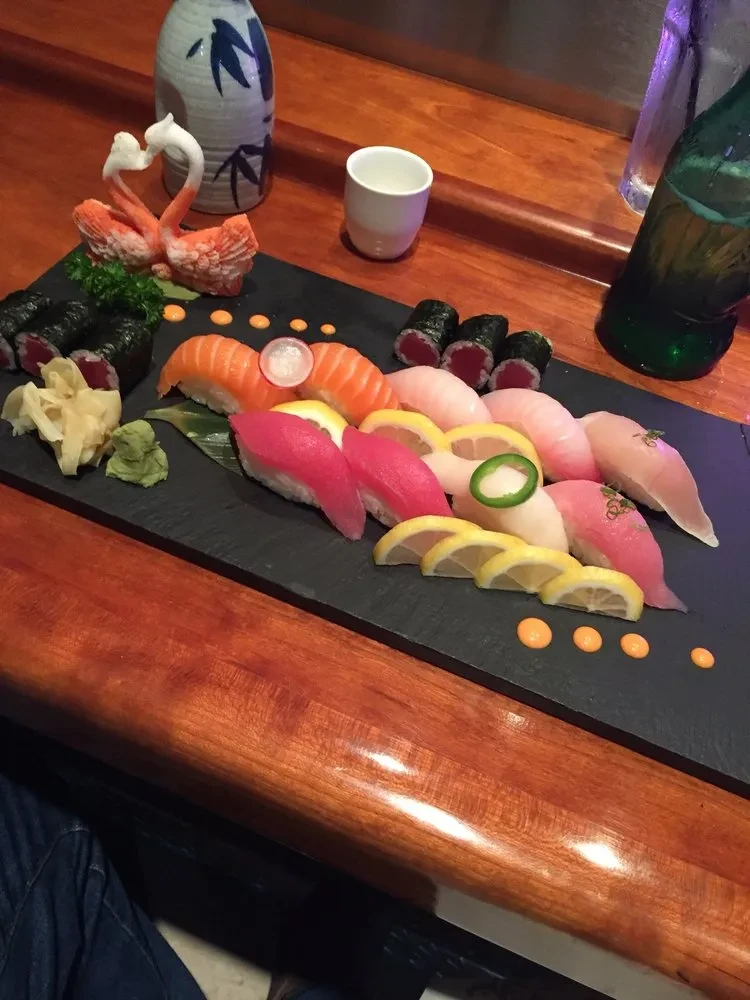 Sushi and sashimi platter with heart-shaped swan carving on black board.