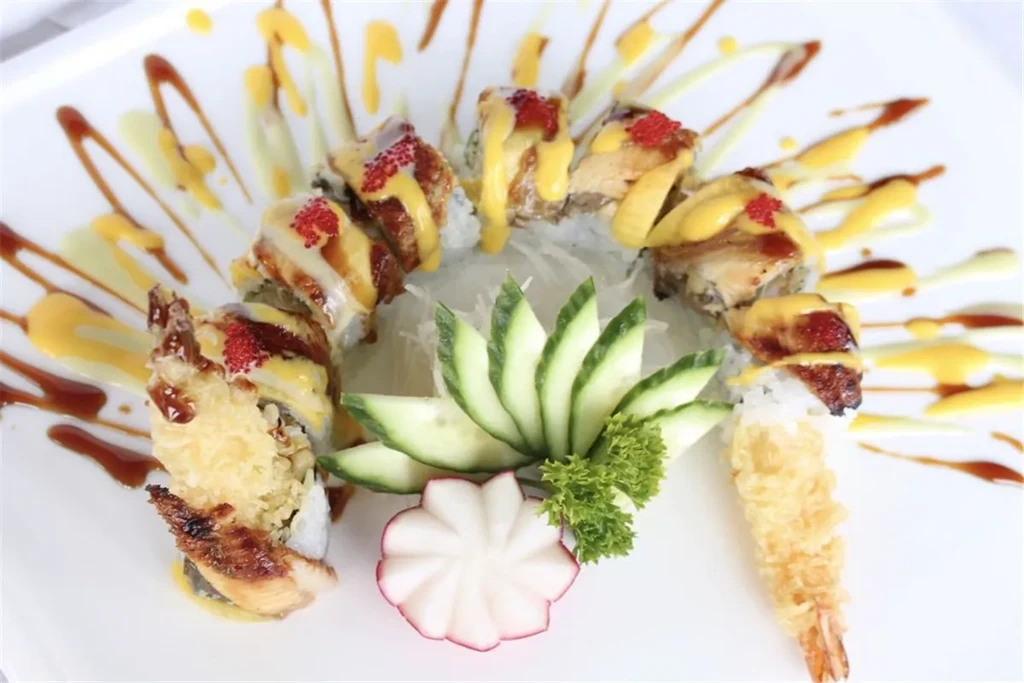 Platter of eel sushi rolls with sauces, red roe, and elaborate garnishes.