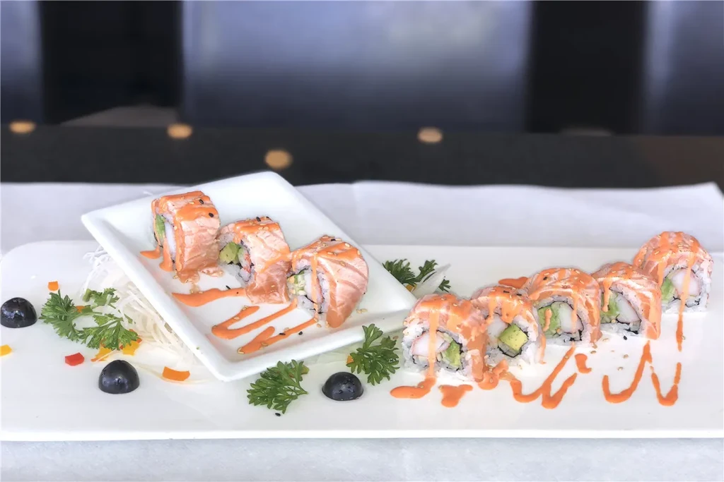 Sushi rolls topped with salmon, orange sauce, sesame, and colorful garnishes.