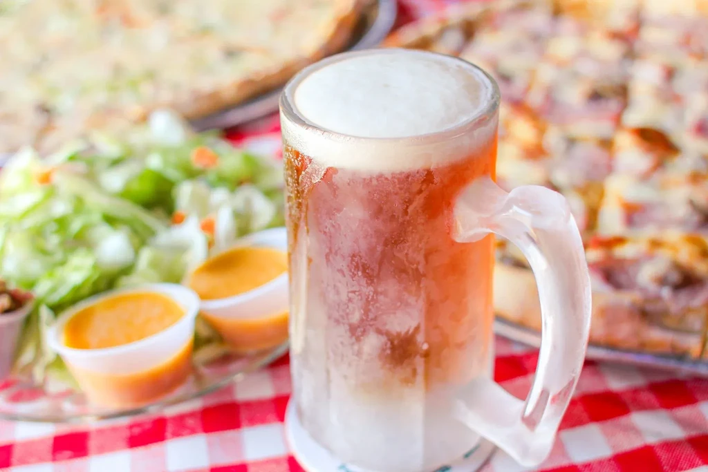Frosty beer mug, thick foam, with blurred salad and pizza.