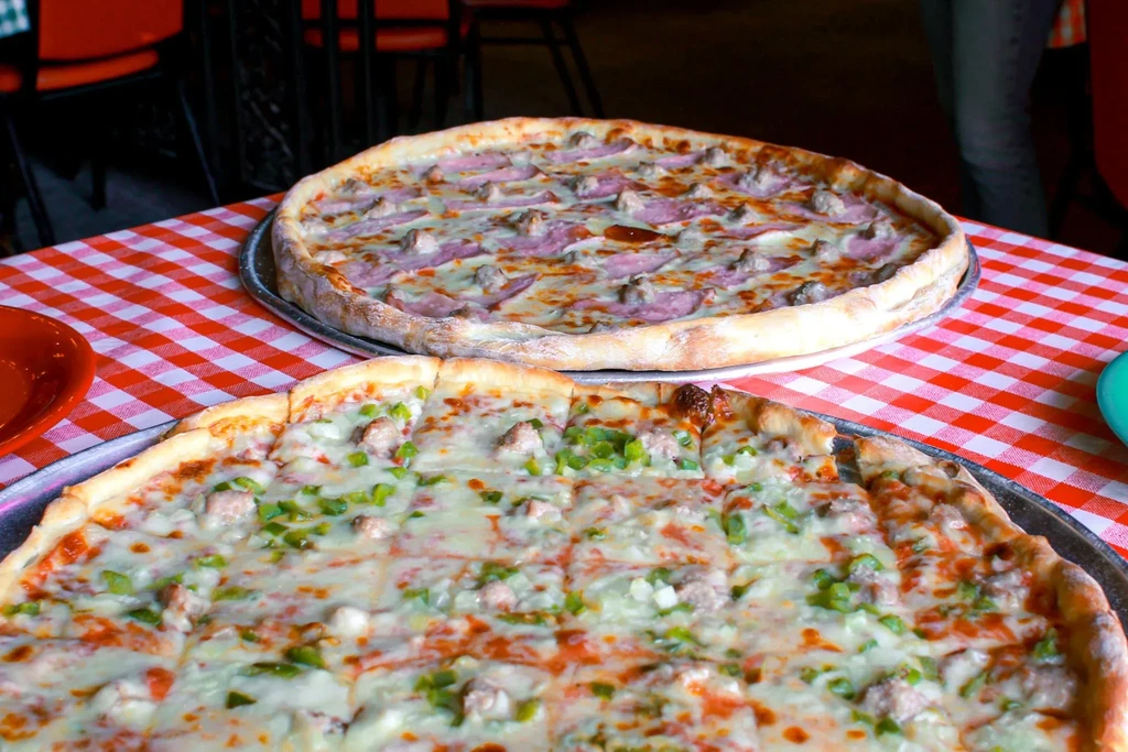 Sliced sausage and whole ham pizzas on a checkered tablecloth.