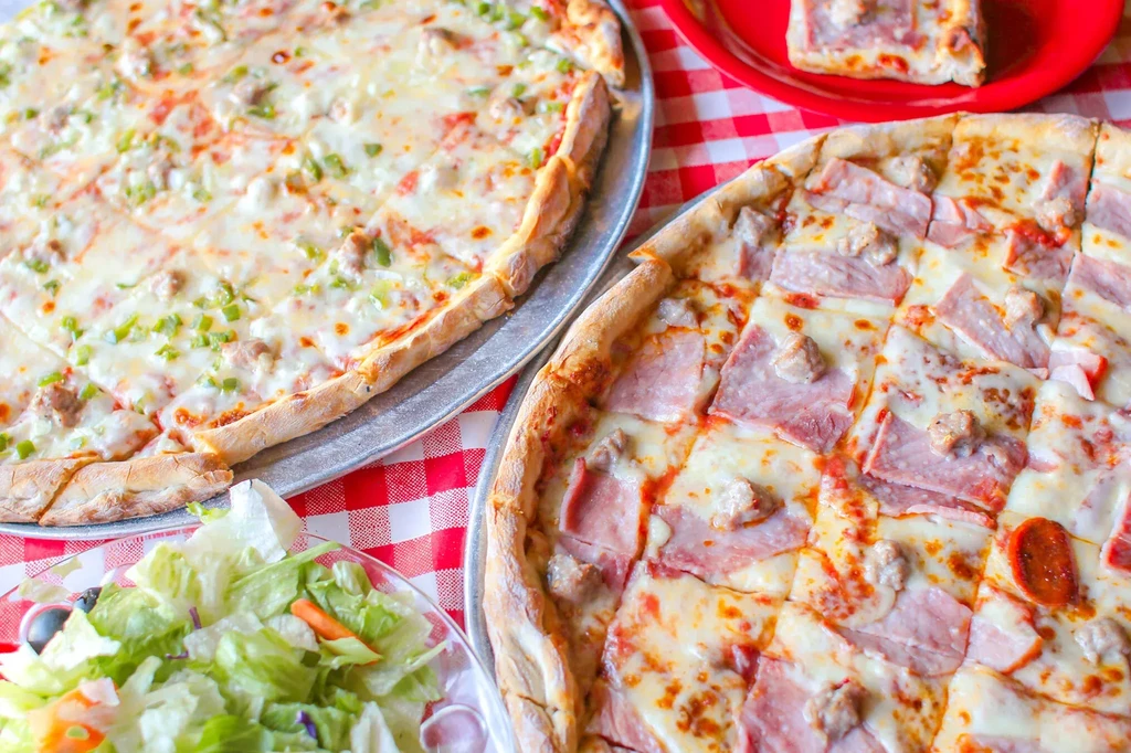 Overhead: Two square-cut pizzas, salad, slice, and checkered table.
