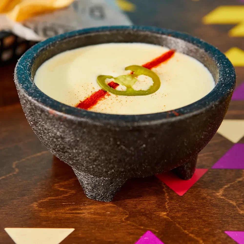 Queso in stone bowl with jalapeño, seasoning, and chips.