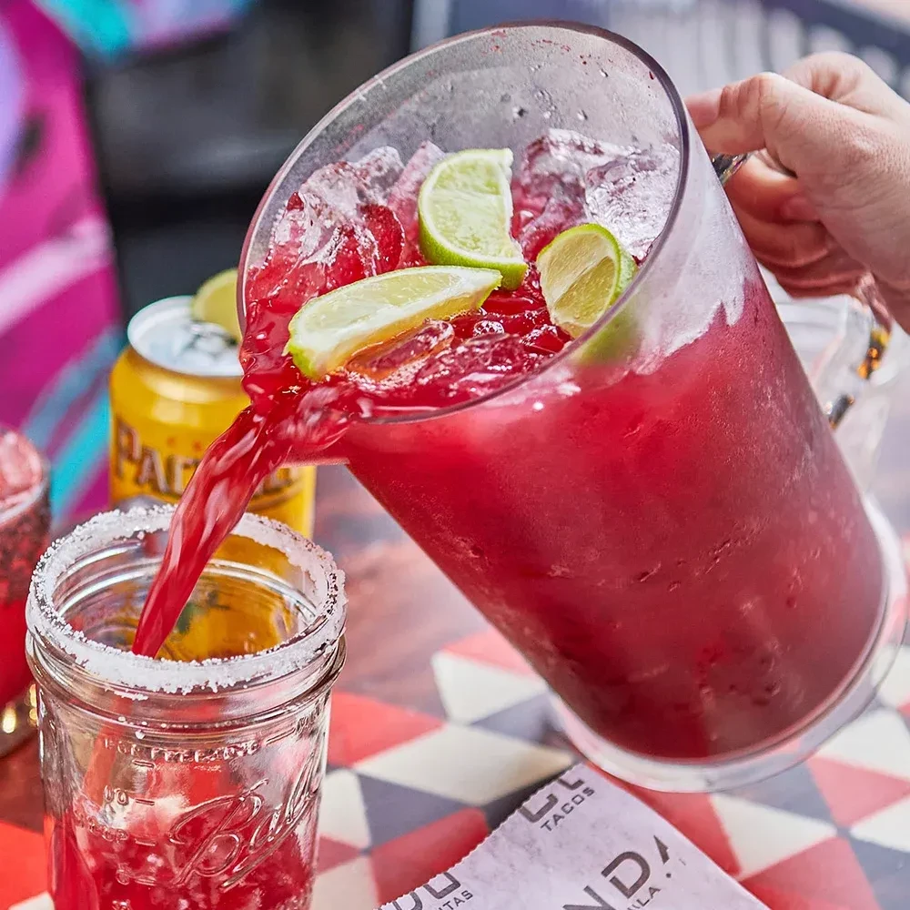 Red icy drink poured from pitcher into salt-rimmed glass with lime.