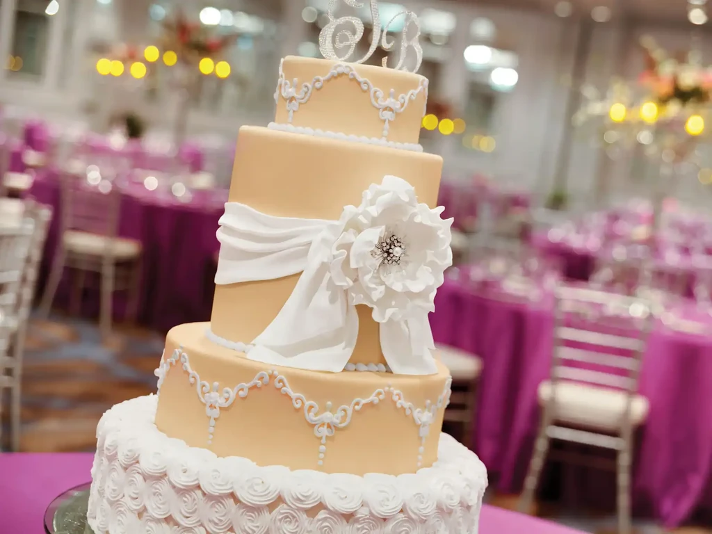 Four-tier cake with peach, white decorations, and 'E&B' initial topper.