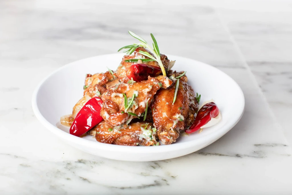 Glazed savory bites, white bowl, creamy sauce, herbs, red elements.