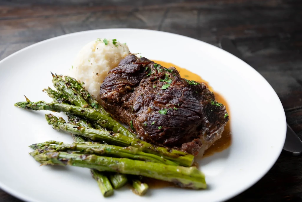 Braised meat, mashed potatoes, and asparagus on a white plate.