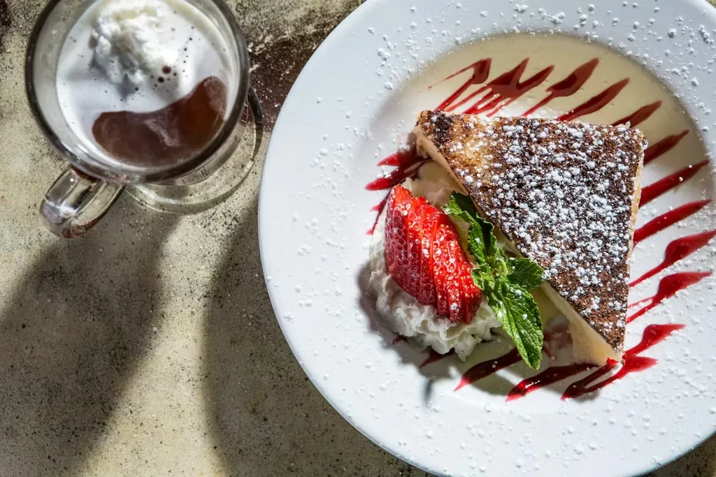 Triangular cheesecake slice with strawberries, whipped cream, and coffee.