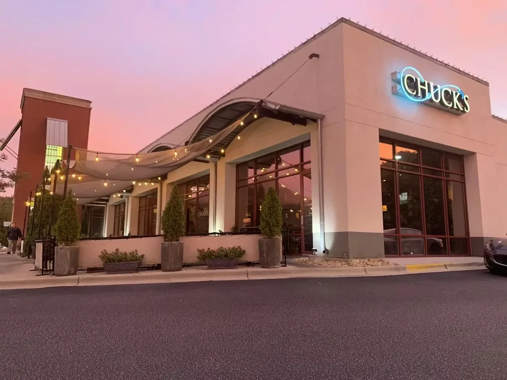 CHUCKS restaurant exterior with glowing sign, patio lights, reflecting pink sky.