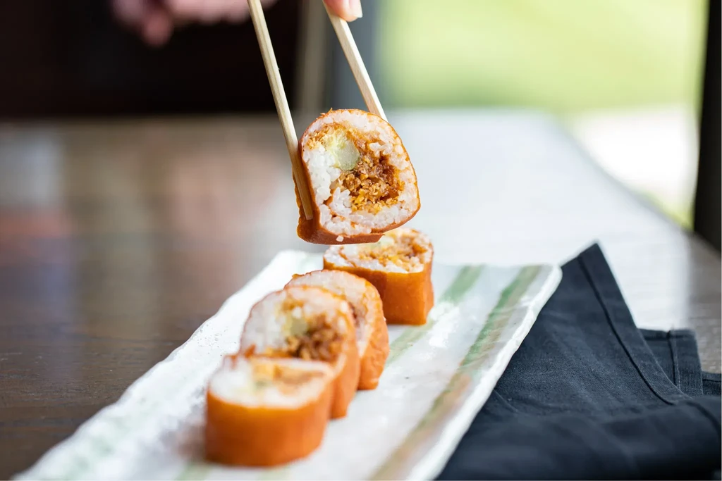 Sushi rolls on a plate, one lifted by chopsticks, revealing filling.
