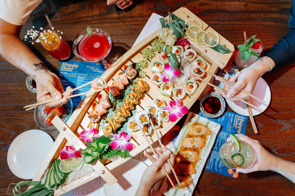 Overhead view: sushi, seared salmon, cocktails, and hands reaching for food.