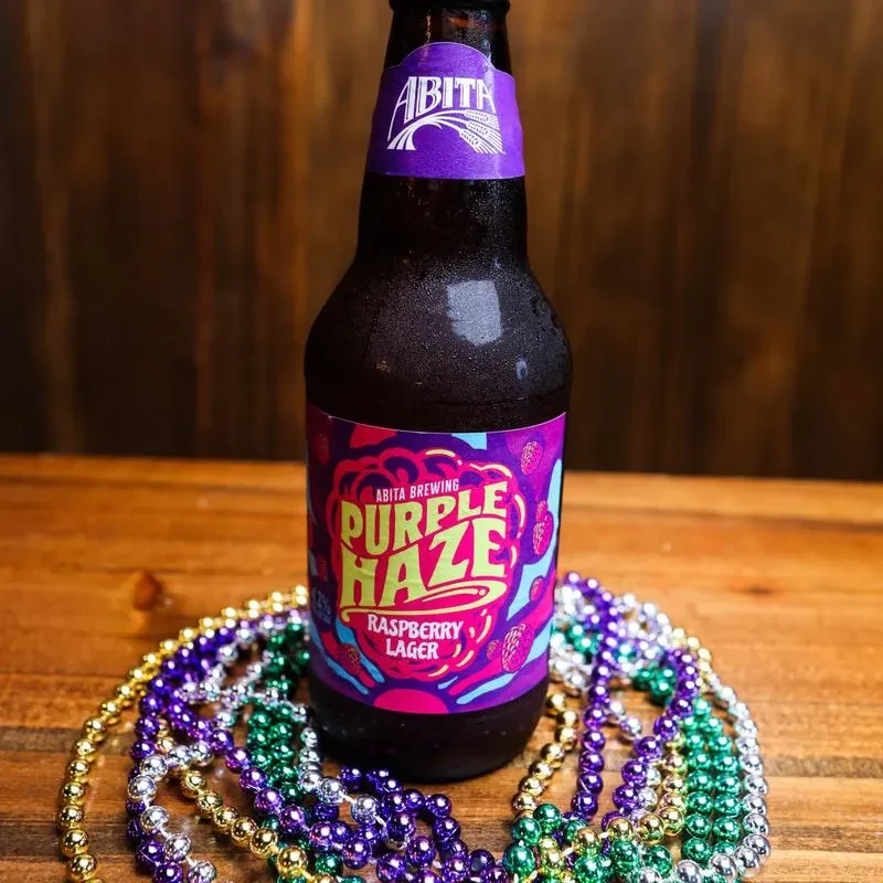 Frosted Abita Purple Haze bottle, Mardi Gras beads on rustic wood.