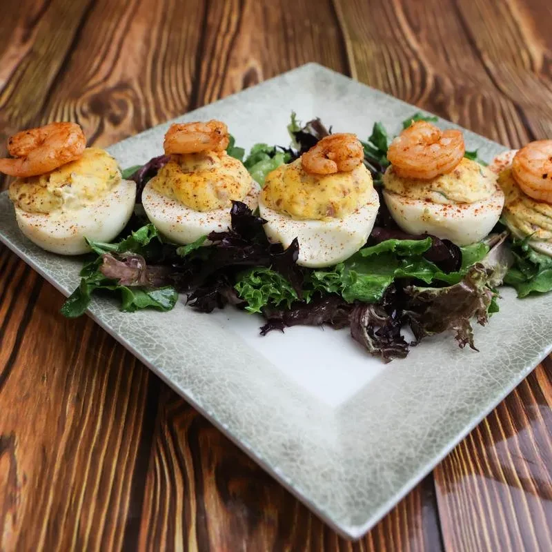 Deviled eggs topped with shrimp and paprika, on mixed greens.