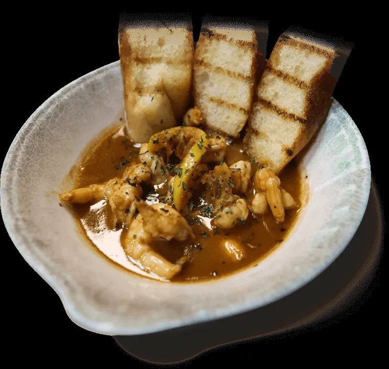 Close-up: shrimp in sauce with lemon, herbs, and grilled bread.