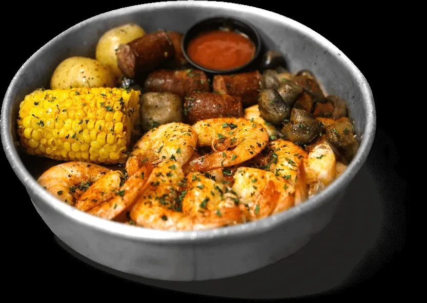 Silver bowl with seasoned shrimp, corn, potatoes, sausage, and mushrooms.