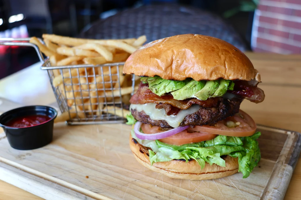An elaborate burger with fries and ketchup on a wooden board.