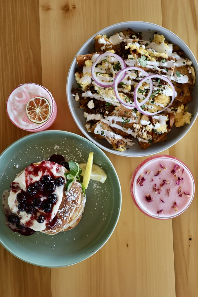 Overhead brunch spread of chilaquiles, pancakes, and two garnished drinks.