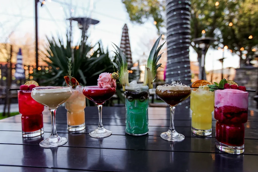 Eight vibrant cocktails with fruit and sorbet on a lit patio.