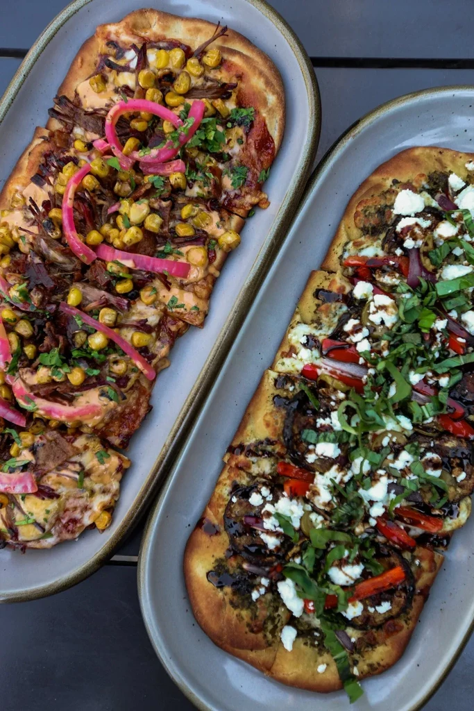 Overhead shot of two rectangular flatbreads with meat and vegetable toppings.