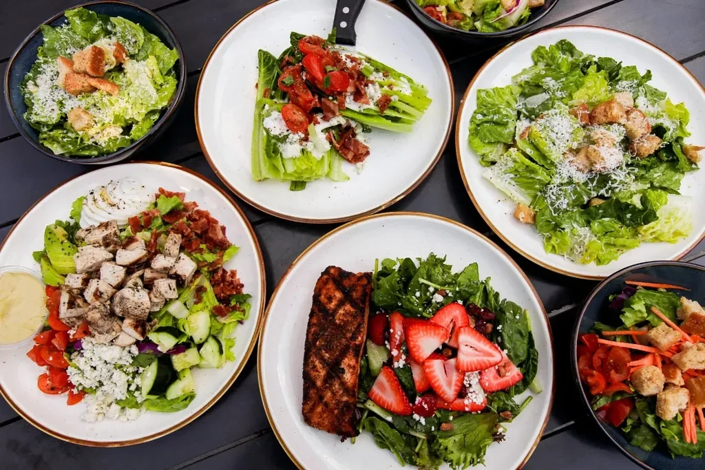 Overhead view of six diverse, colorful salads on plates and in bowls.