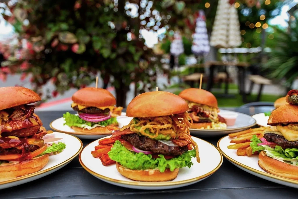 Gourmet hamburgers with sides on plates at an outdoor restaurant.