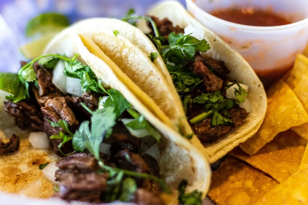 Two street tacos filled with meat, onions, cilantro, and lime.
