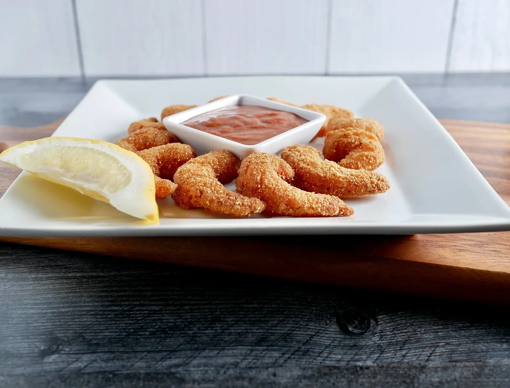 Golden fried seafood with reddish dipping sauce and a lemon wedge.
