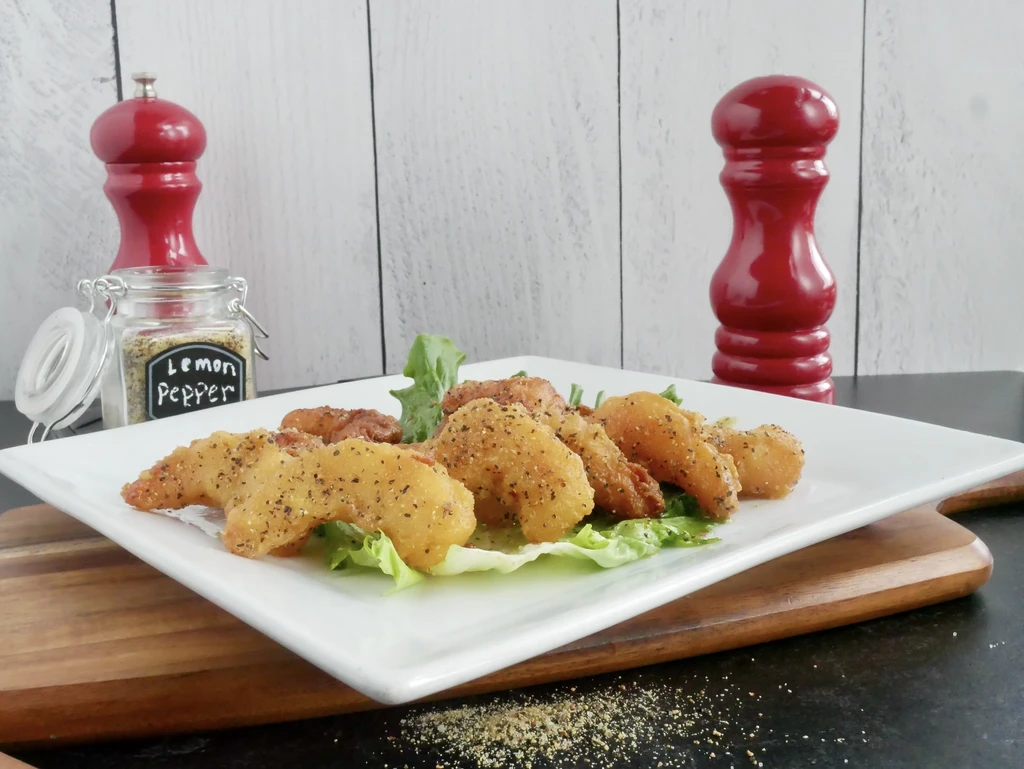 Golden-brown breaded shrimp on lettuce, wooden board, with spices nearby.