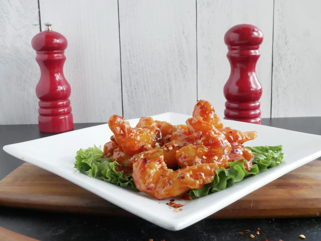 Plate of cooked shrimp with orange-red sauce, lettuce, pepper flakes.
