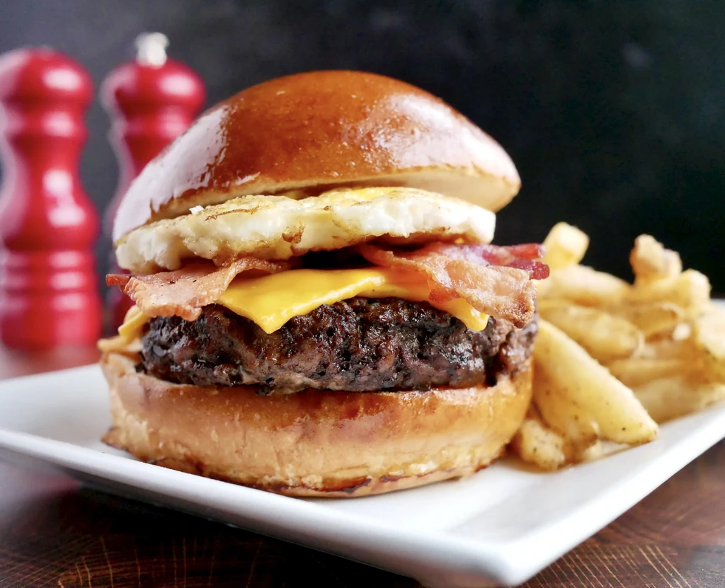 Char-grilled burger with melted cheese, bacon, fried egg, and fries.
