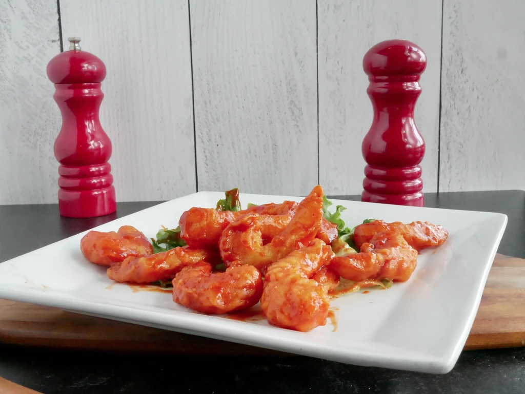 Plate of crispy shrimp with orange-red sauce on lettuce.