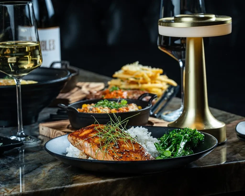 Pan-seared salmon with rice, wine, and fries on a dining table.
