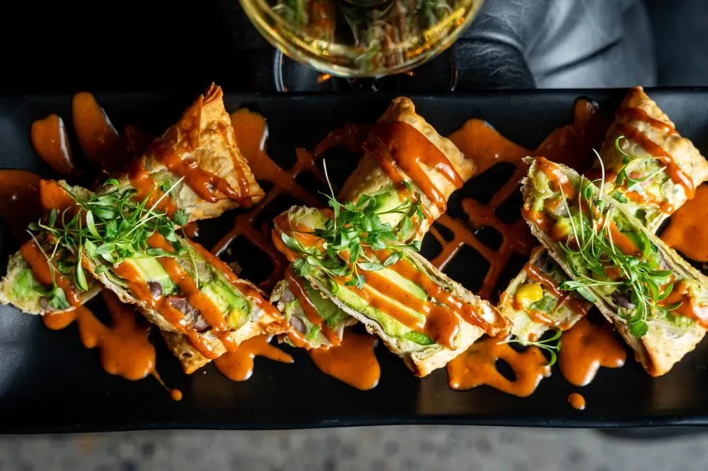 Crispy avocado, corn, and bean triangles with sauce and microgreen garnish.