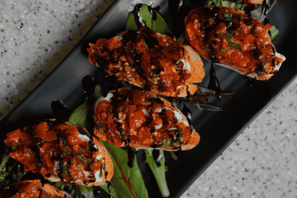 Five bruschetta topped with tomatoes, herbs, cheese, and balsamic glaze.