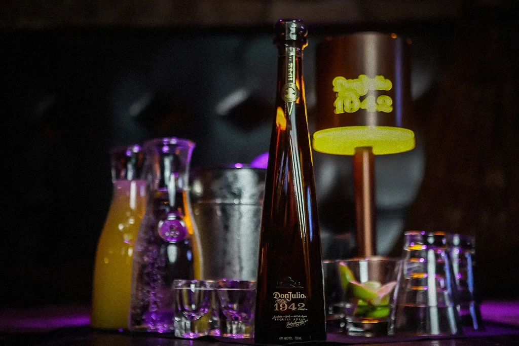 Don Julio 1942 tequila bottle, carafes, and glasses on a dark bar.