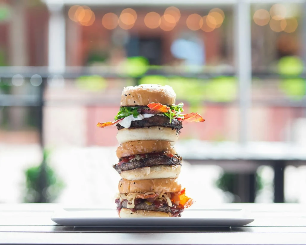 Extremely tall, three-layer burger with bacon, lettuce, and sauces.