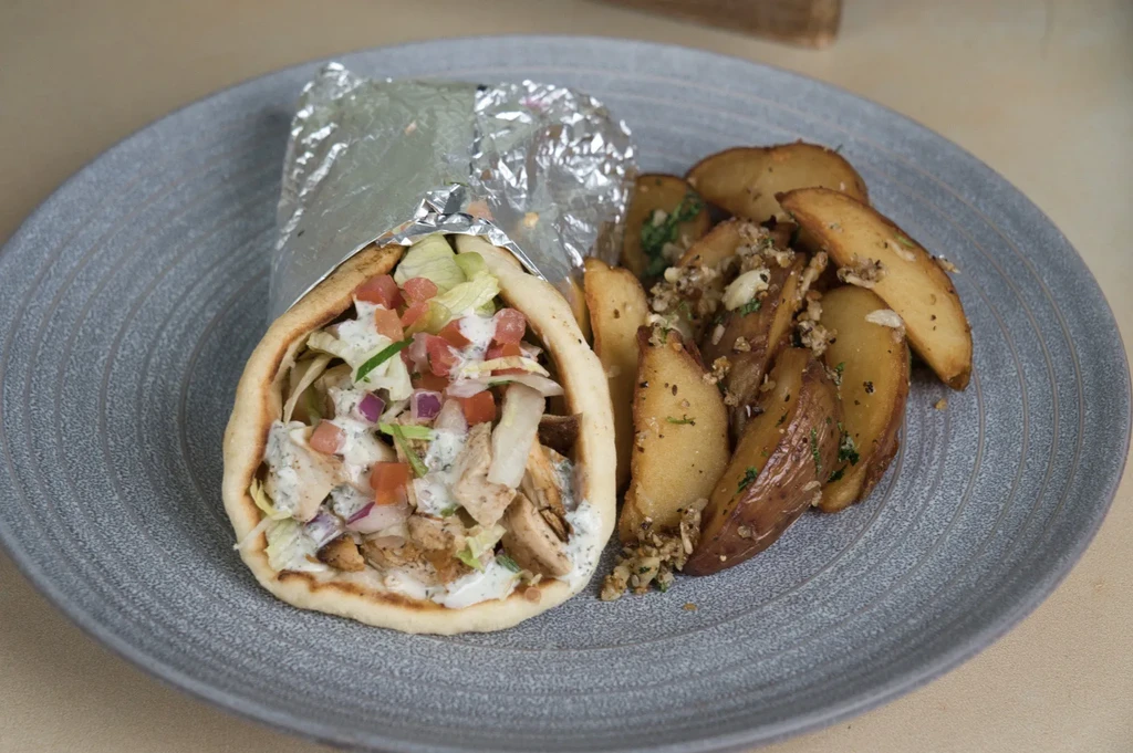 Partially unwrapped pita wrap with meat, vegetables, and potato wedges.