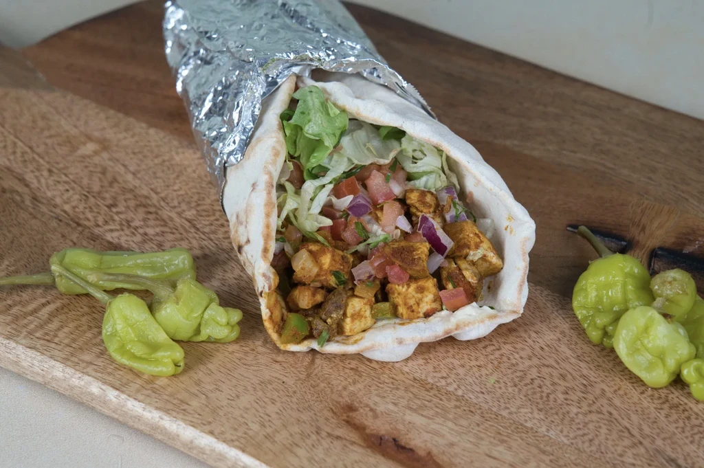 Partially unwrapped burrito with chicken, vegetables, and peppers on wood.