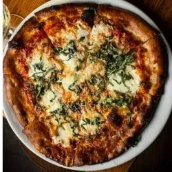 Freshly baked pizza, cut, with melted cheese, basil, and tomato sauce.