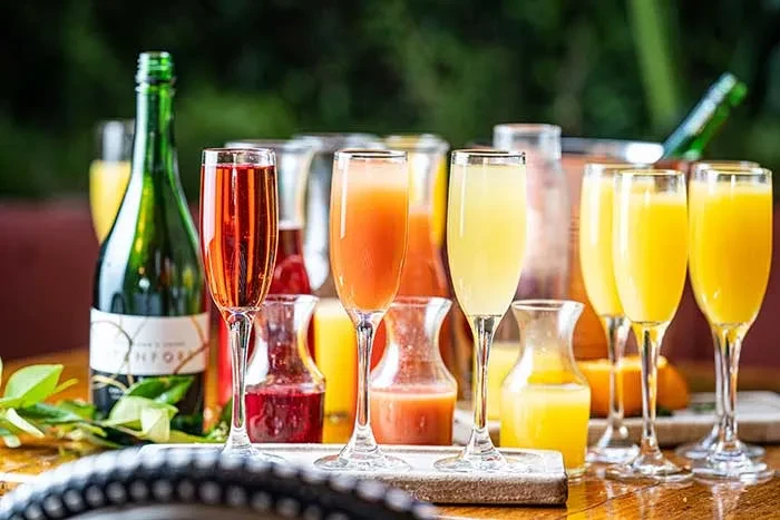 Vibrant mimosa bar with colorful drinks, flutes, and juice carafes.