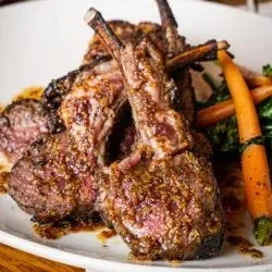 Roasted lamb chops with glazed carrots and green vegetables on a white plate.
