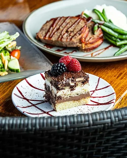 Layered chocolate cake with berries; blurred main course and salad.