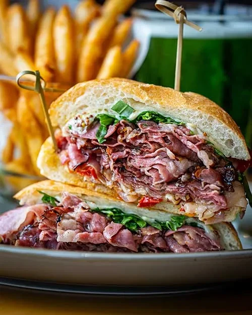 Close-up of a stacked meat sandwich with lettuce, sauce, and fries.