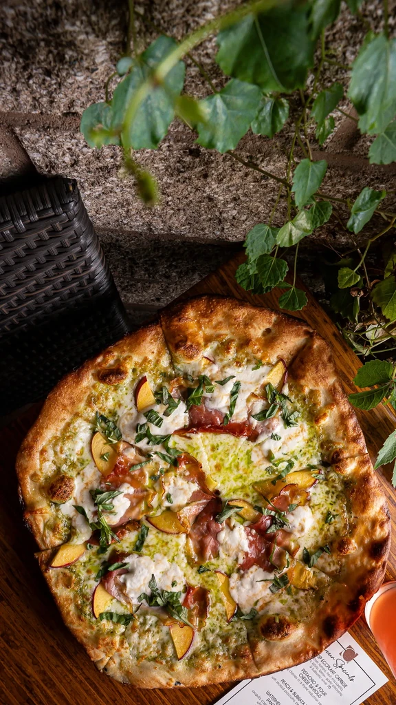 Pizza topped with pesto, creamy cheese, prosciutto, peaches, and basil.