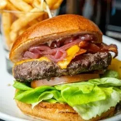 Gourmet hamburger with beef, cheese, bacon, lettuce, tomato, and fries.