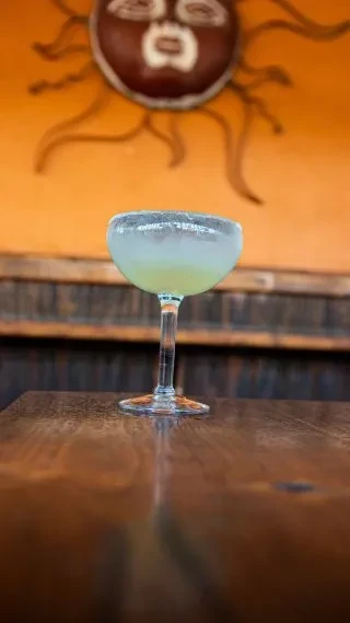 Cold sugared-rim cocktail in coupe glass on table, orange wall.